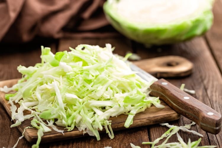 Shredded cabbage on a board next to a knife and a whole cabbage