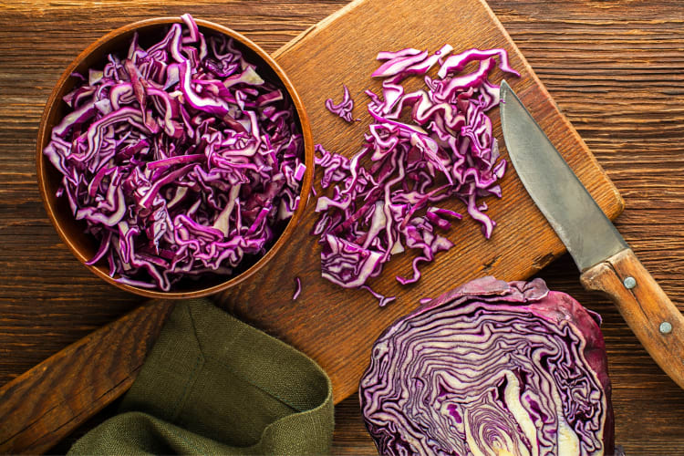 Red cabbage on a chopping board next to a bowl of shredded red cabbage