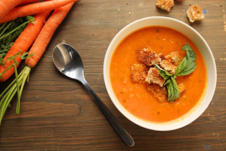 Carrot soup with croutons next to fresh carrots