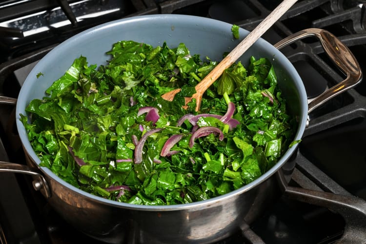 Kale pieces being cooked with onions in a pot on a stove