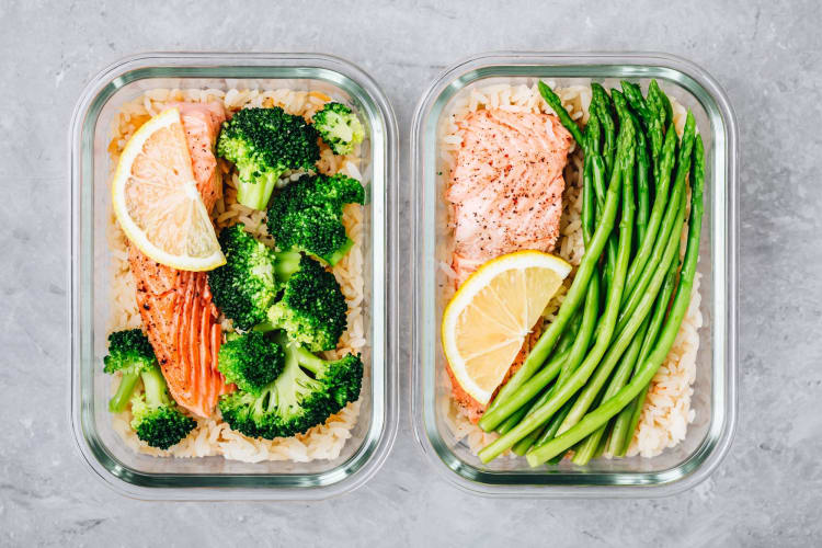 Meal prep lunch box containers with baked salmon fish, rice, green broccoli and asparagus.