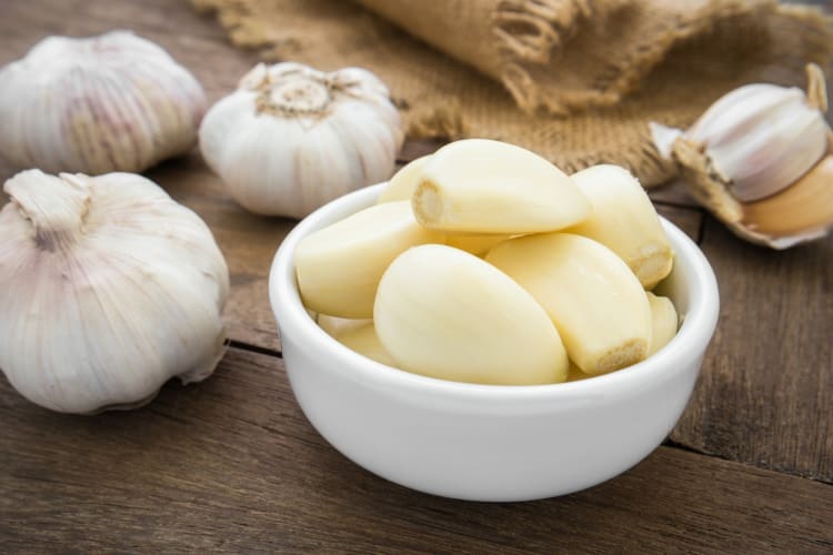 Garlic cloves in a bowl next to bulbs of garlic