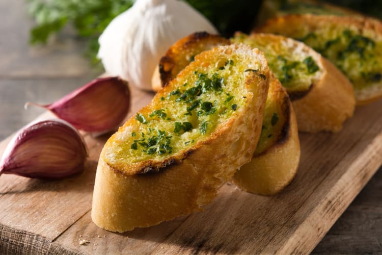 Garlic bread on a board next to garlic