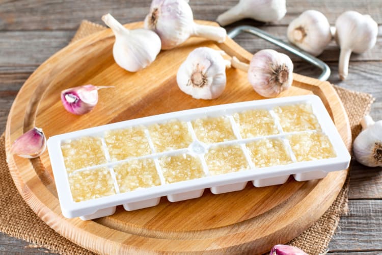 Frozen garlic in an ice cube tray next to fresh garlic