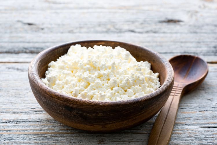 Ricotta cheese in a wooden bowl next to a wooden spoon