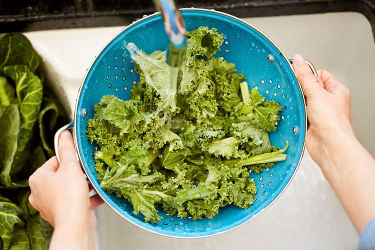Aerial shot of kale being washed in a bowl, under a tap