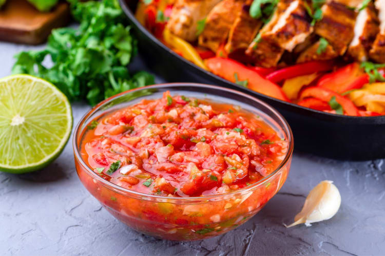 A bowl of salsa and half a lime next to a meat and vegetable dish