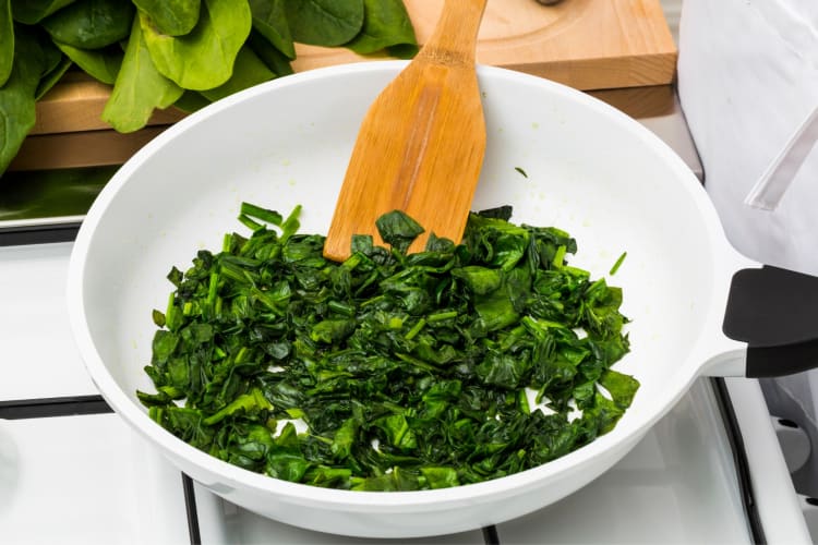 A person cooking spinach in a pan