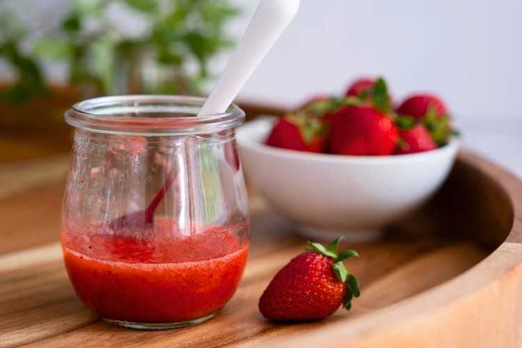 A jar of strawberry puree next to strawberries