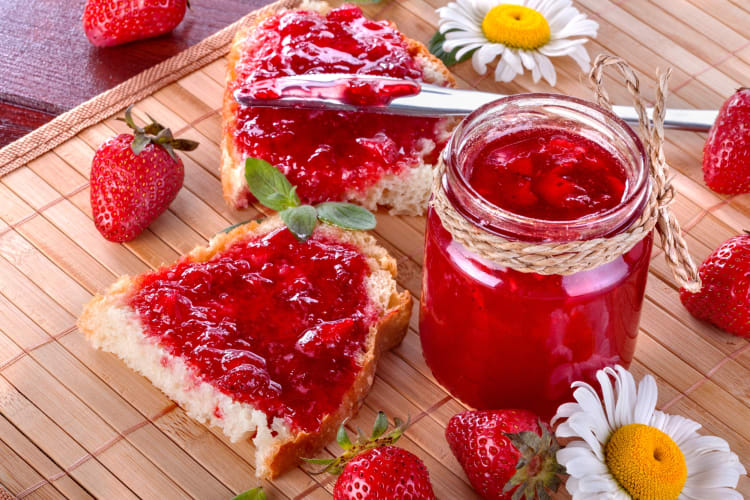 A jar of strawberry jam next to flowers and strawberries