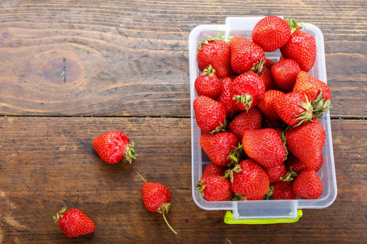 Strawberries in a plastic container on a wooden surface