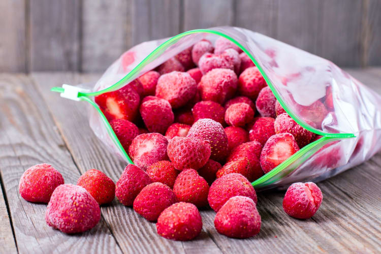 Whole frozen strawberries in and around a plastic freezer bag