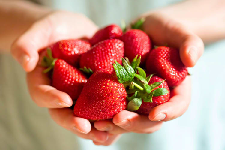 A person holding whole strawberries in their hands