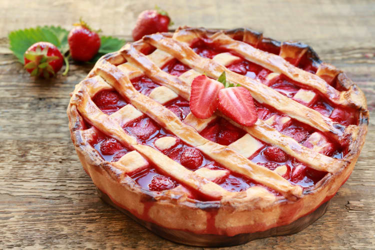 A strawberry pie on a wood surface next to fresh strawberries