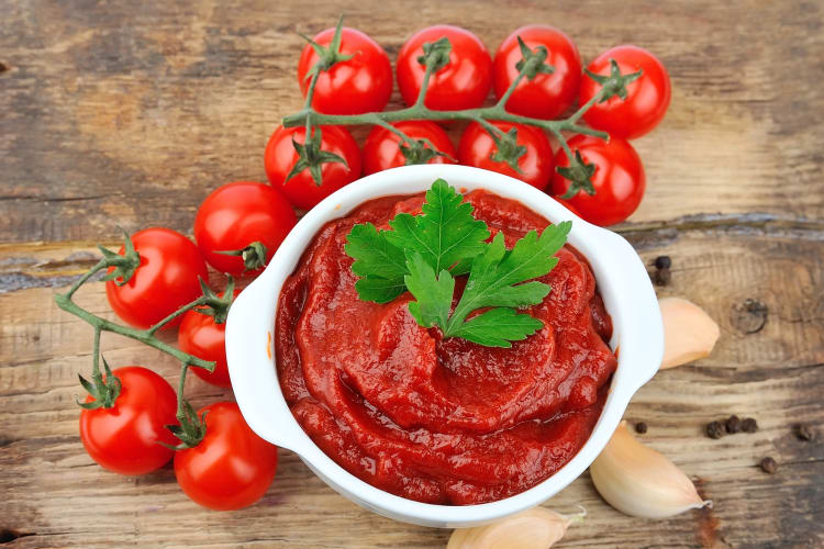 Tomato paste in a bowl next to tomatoes