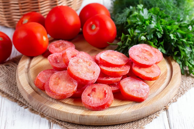 Frozen whole and sliced tomatoes on a wooden board