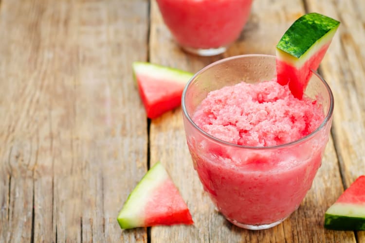 A cup with pureed watermelon next to watermelon slices