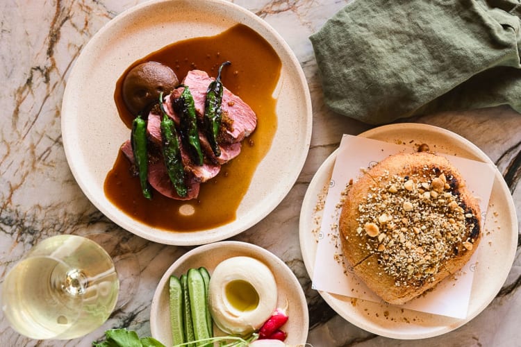 A glass of wine, entrée, dessert and side dish on a restaurant table.