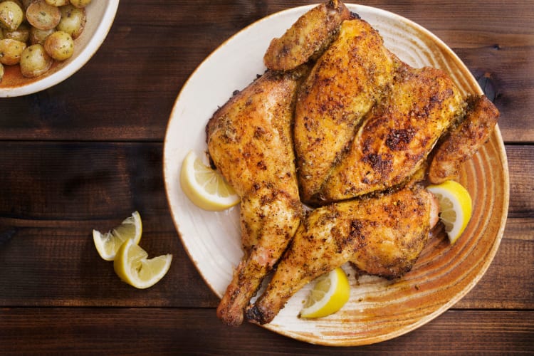 A spatchcock chicken with a side dish of potatoes.