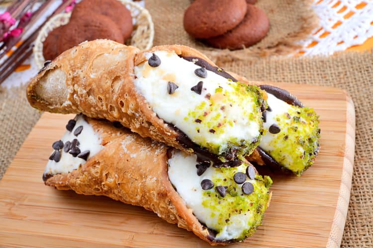 Three portions of cannoli on a wooden serving board