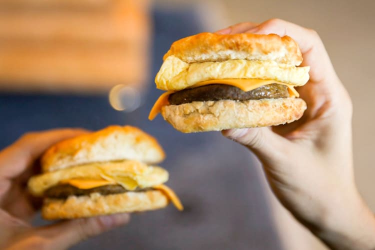 Two people holding breakfast sandwiches
