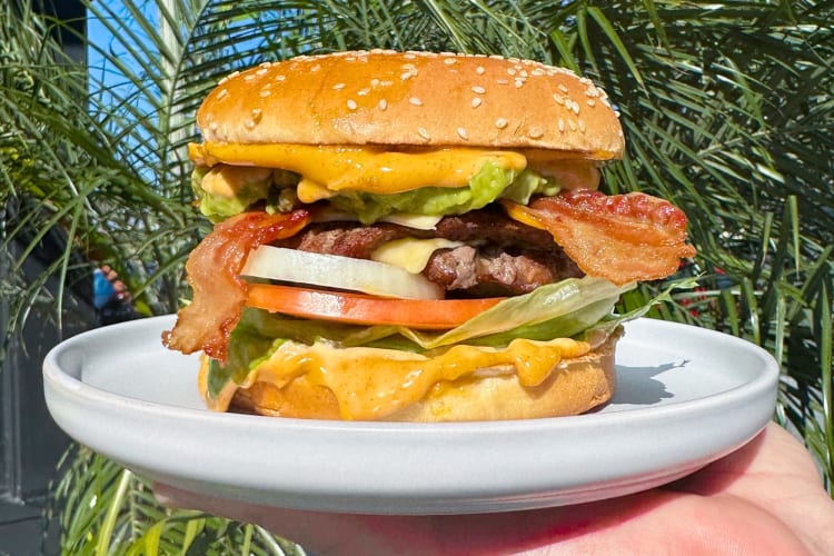A person holding a burger with bacon, cheese and other fillings