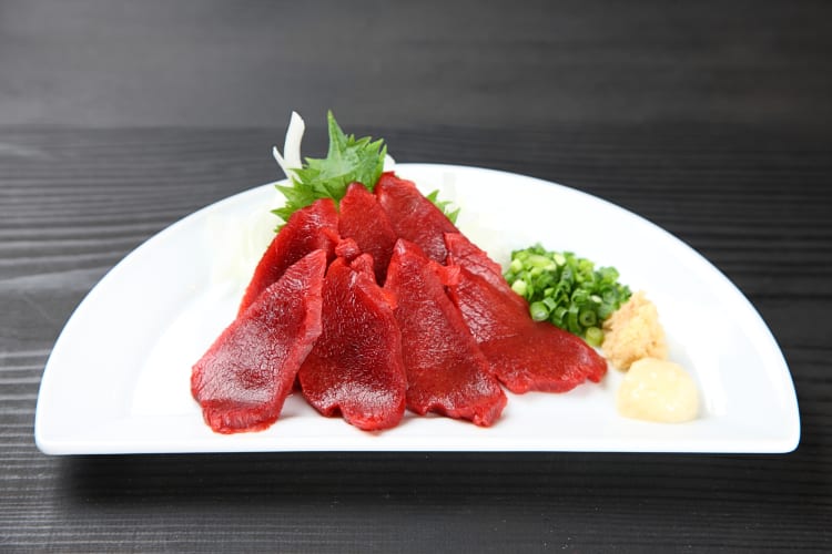 Horse meat sashimi on a plate with bits of spring onion, ginger and garlic