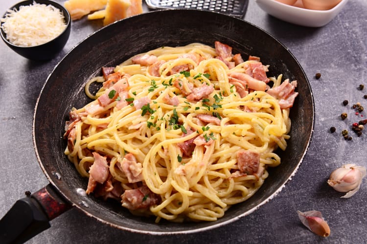 Carbonara in a pan, next to grated cheese in a bowl
