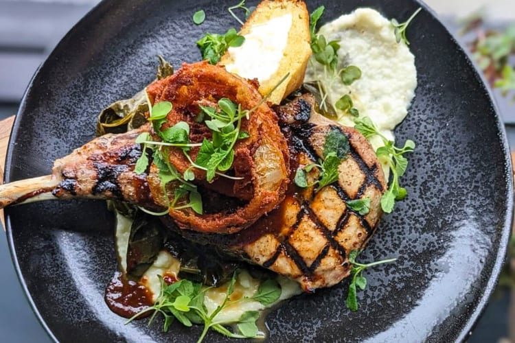 Aerial view of a pork chop pickled jalapeño cheddar grits, collard greens, roadhouse BBQ and an cornbread onion ring