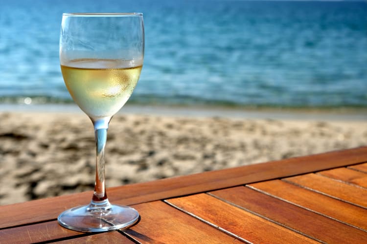 Glass of white wine on a wooden deck in front of the beach