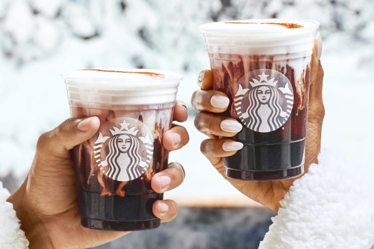 Two people holding Starbucks coffee drinks