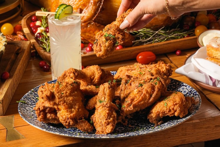 A person taking a piece of Yardbird fried chicken from a plate