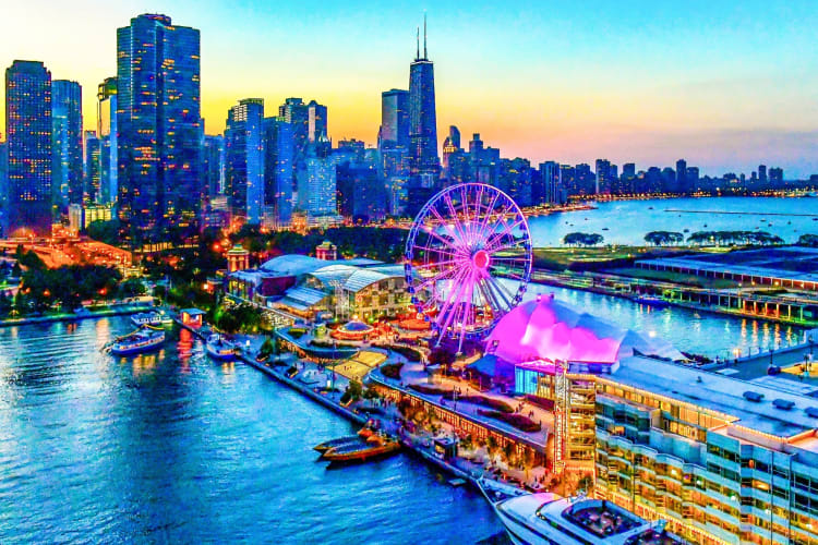 A pier, buildings and a Ferris wheel illuminated at night