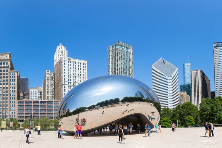 A bean-shaped reflective sculpture in a square next to buildings