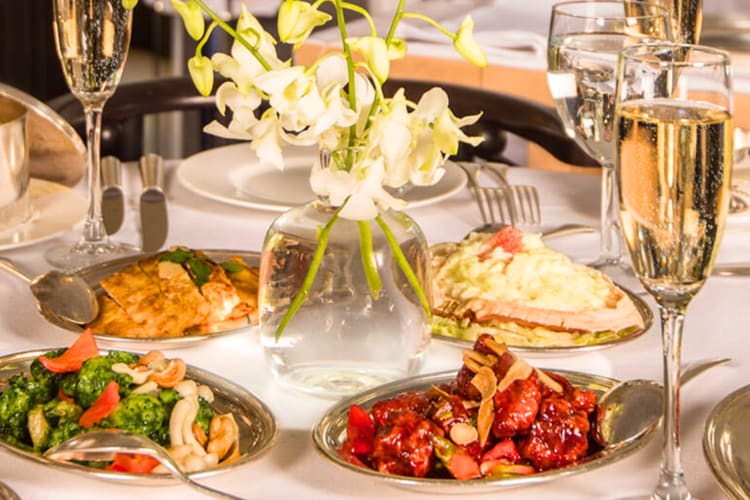 A selection of Chinese dishes and Champagne glasses on a table with flowers
