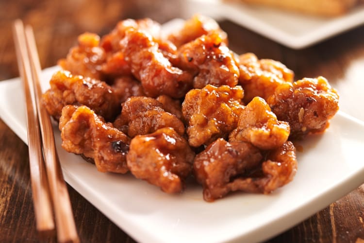 Orange chicken on a plate next to chopsticks
