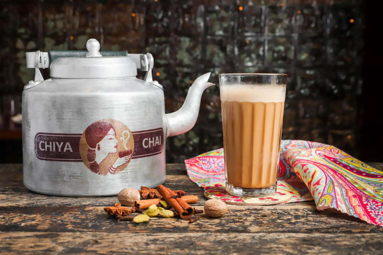 Chiya Chai Café pot next to chai in a glass, with herbs in front of them