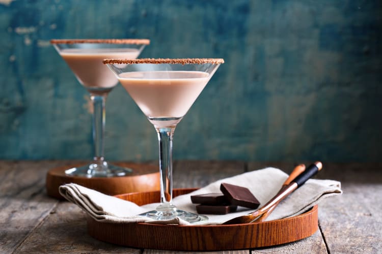 Two chocolate martinis on wooden surfaces, with spoons and blocks of chocolate