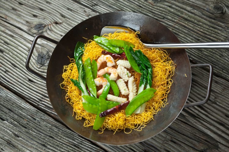 A wok with Chinese chow mein with shrimp and greens.
