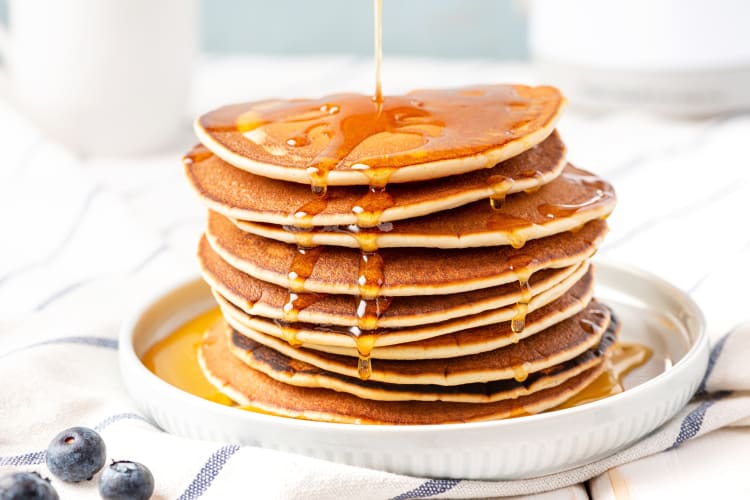 Large stack of pancakes with syrup being poured over them