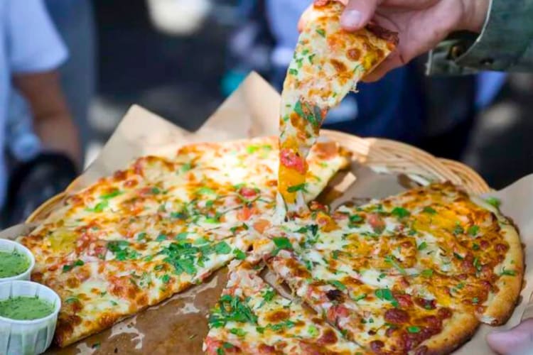 A person taking a slice of pizza from a whole pie