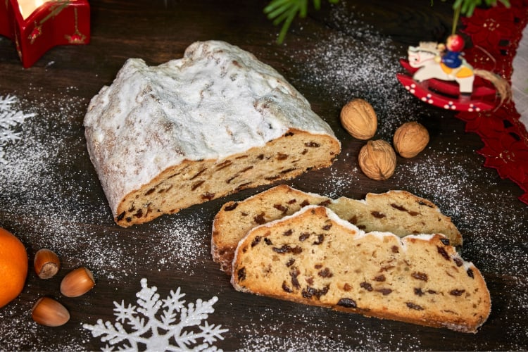 A fruit cake covered in powdered sugar next to Christmas decorations