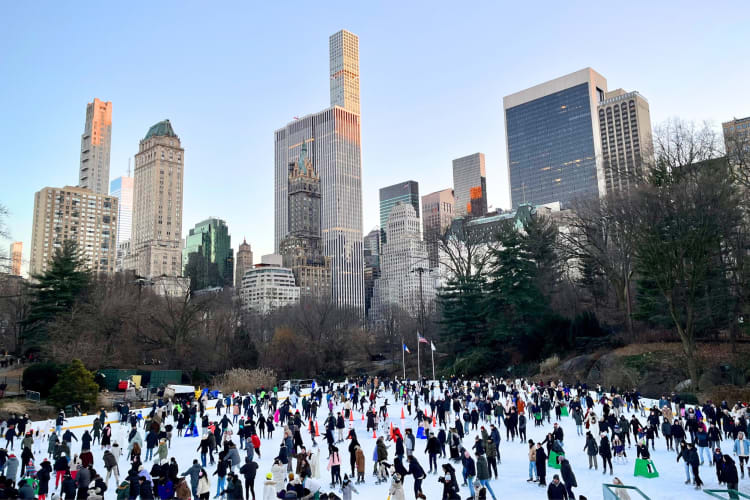 People skating on an outdoor ice rink next to city buildings