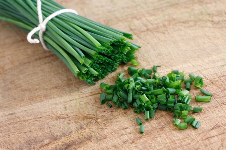 A bunch of chives and chopped chives on a board