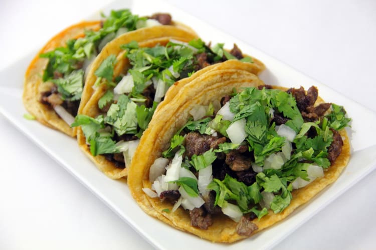 Three tacos filled with onions, beef and cilantro