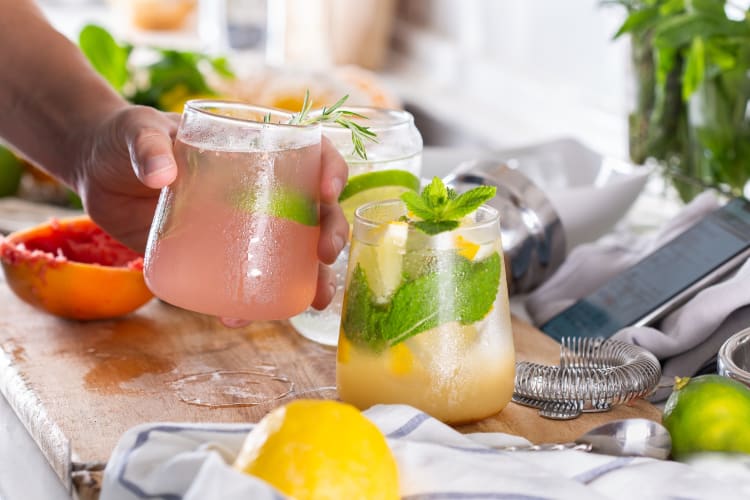 A person picking up a cocktail next to citrus fruits