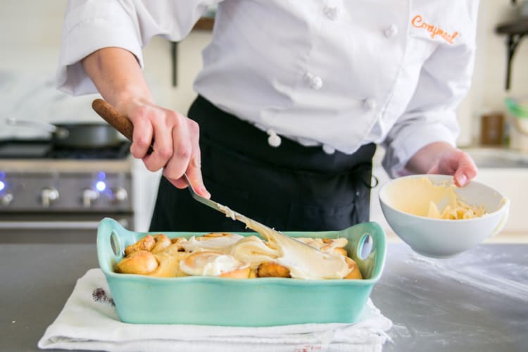 A person in a Cozymeal apron frosting cinnamon buns