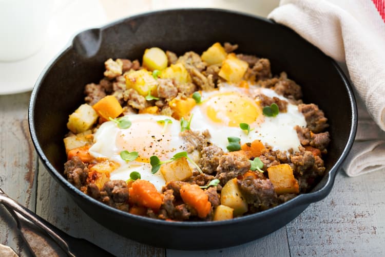Potato and sweet potato hash with eggs in a cast iron pan