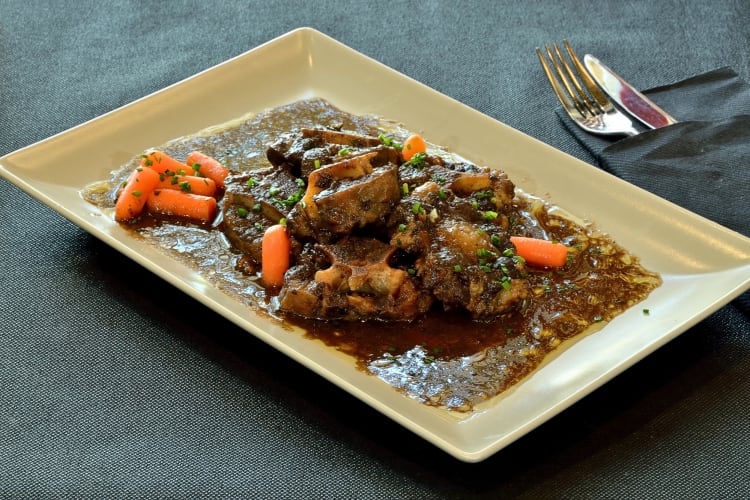 Coda Alla Vaccinara on a plate next to a knife, fork and napkin
