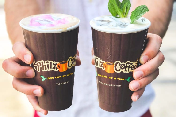 A person holding two brown takeout coffee cups